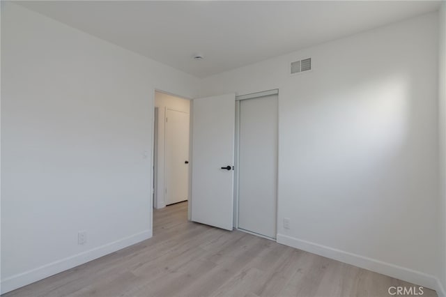 unfurnished bedroom featuring light wood-type flooring, baseboards, visible vents, and a closet