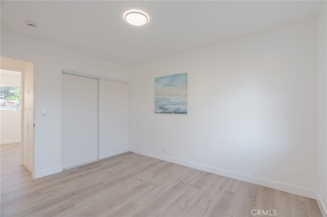 unfurnished bedroom featuring light wood finished floors, baseboards, and a closet