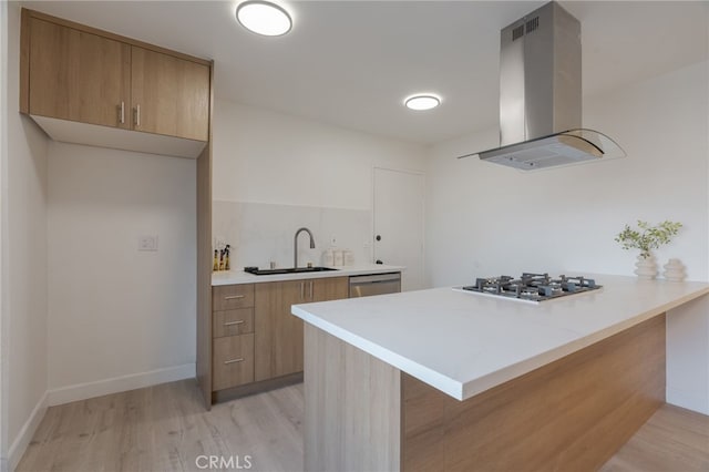 kitchen featuring light countertops, appliances with stainless steel finishes, a sink, island range hood, and a peninsula