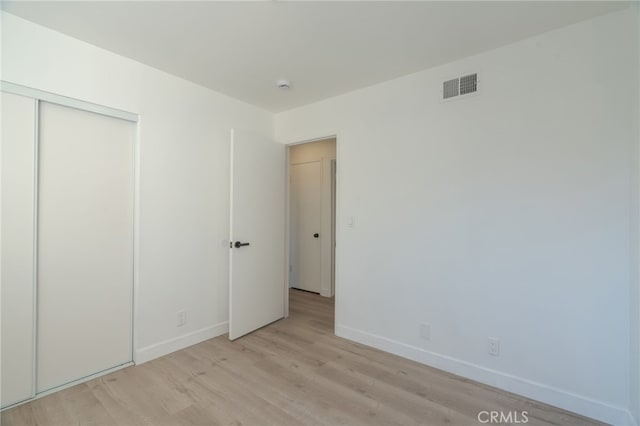 unfurnished bedroom featuring a closet, baseboards, visible vents, and light wood finished floors