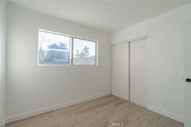 unfurnished bedroom with light wood-type flooring, a closet, and baseboards