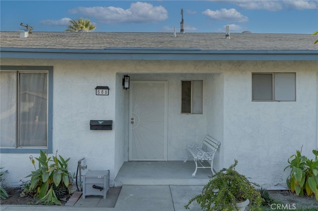 doorway to property featuring roof with shingles, a patio area, and stucco siding