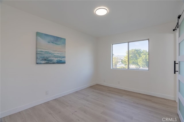 spare room featuring light wood-type flooring, a barn door, and baseboards