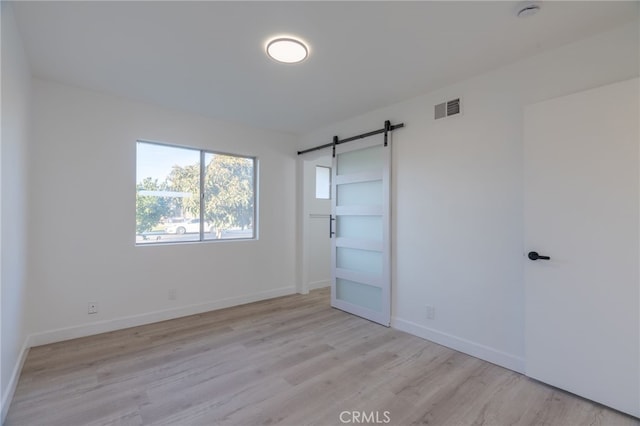 empty room with light wood finished floors, a barn door, visible vents, and baseboards