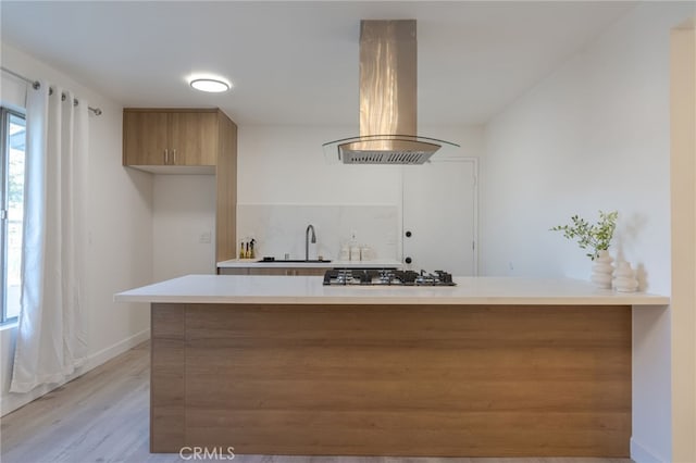 kitchen with stainless steel gas cooktop, light countertops, island range hood, modern cabinets, and a peninsula