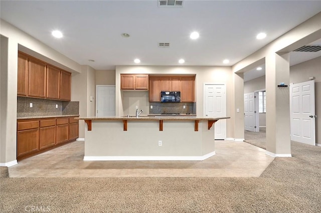 kitchen with a kitchen bar, light carpet, a center island with sink, and backsplash