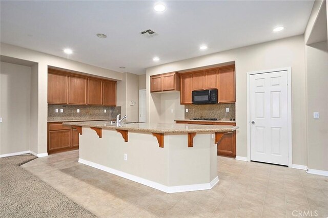 kitchen featuring tasteful backsplash, sink, a kitchen breakfast bar, a kitchen island with sink, and light stone counters