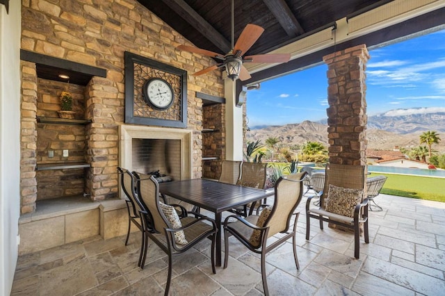 view of patio with ceiling fan, a mountain view, and an outdoor stone fireplace