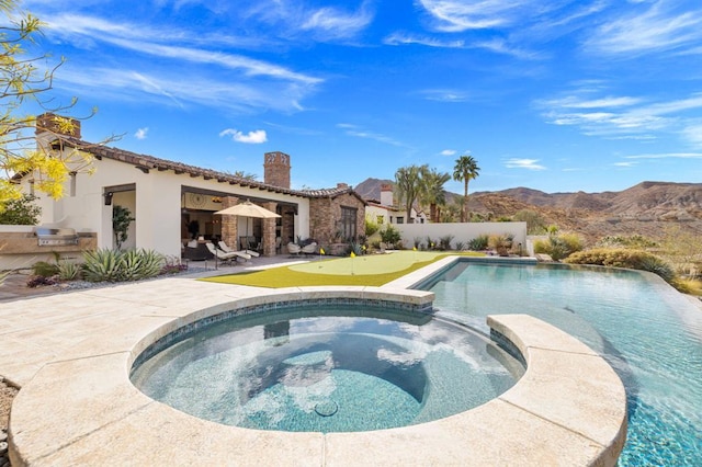 view of swimming pool featuring a mountain view, a patio area, an in ground hot tub, and an outdoor kitchen