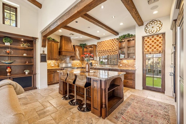 kitchen featuring a breakfast bar, backsplash, custom exhaust hood, a center island, and light stone countertops