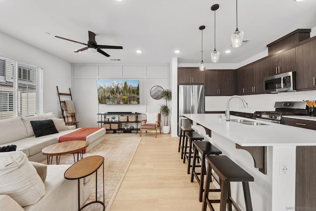 kitchen featuring sink, appliances with stainless steel finishes, dark brown cabinets, a kitchen bar, and decorative light fixtures