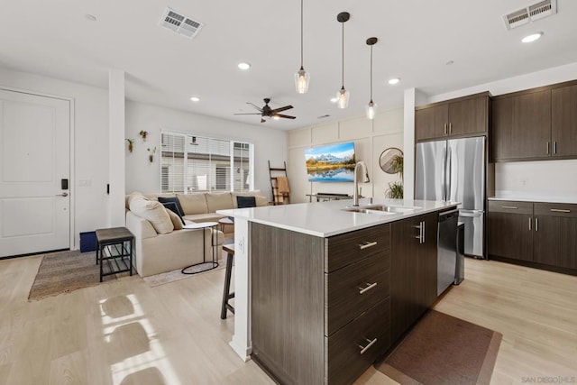 kitchen with sink, appliances with stainless steel finishes, dark brown cabinets, a center island with sink, and light wood-type flooring