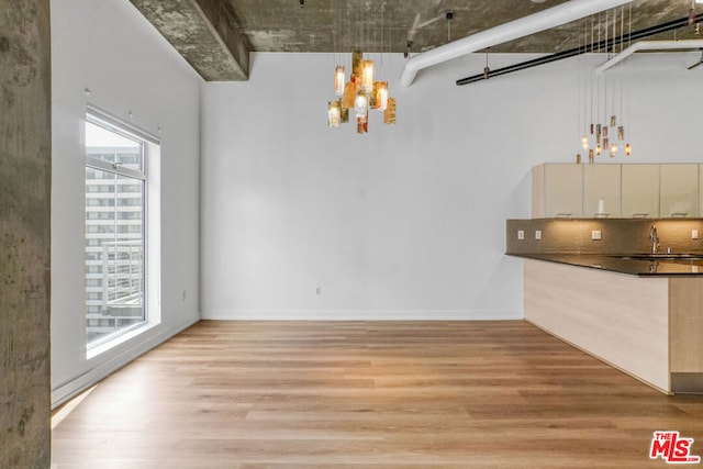 unfurnished dining area featuring sink, an inviting chandelier, and light wood-type flooring