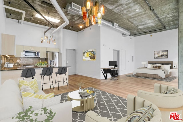 living room with sink, light wood-type flooring, and a high ceiling