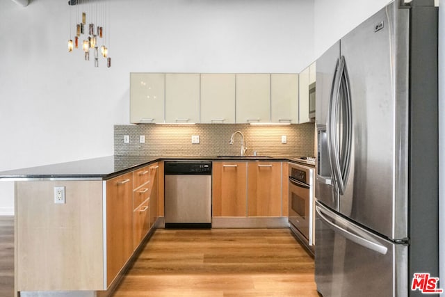 kitchen with sink, appliances with stainless steel finishes, backsplash, light hardwood / wood-style floors, and kitchen peninsula