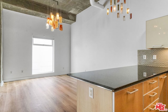 kitchen featuring pendant lighting, backsplash, dark stone counters, and light wood-type flooring