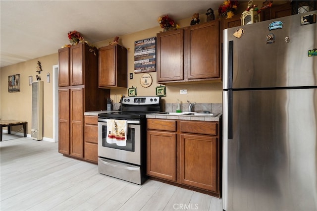 kitchen with appliances with stainless steel finishes, tile counters, sink, and light wood-type flooring