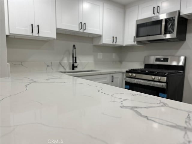 kitchen with light stone counters, appliances with stainless steel finishes, and white cabinets