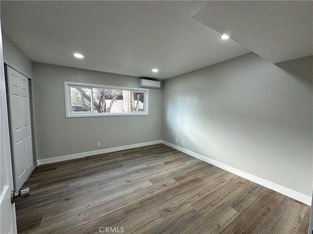 unfurnished bedroom featuring a wall mounted air conditioner, hardwood / wood-style floors, and a closet