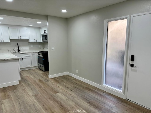 kitchen featuring appliances with stainless steel finishes, sink, white cabinets, light stone counters, and light hardwood / wood-style floors