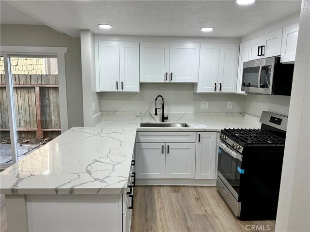 kitchen featuring sink, white cabinetry, light stone counters, appliances with stainless steel finishes, and kitchen peninsula