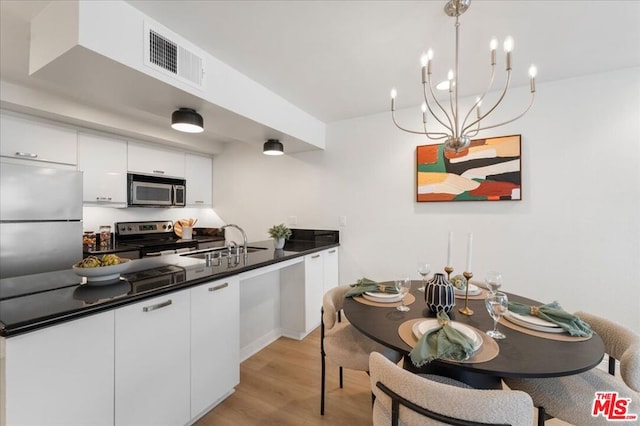 kitchen featuring decorative light fixtures, white cabinetry, sink, light hardwood / wood-style floors, and stainless steel appliances