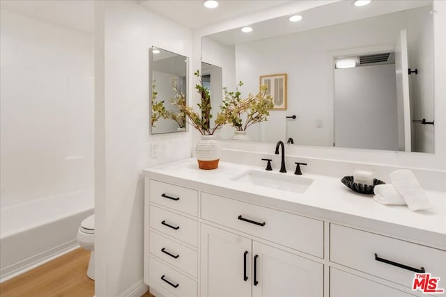 full bathroom with hardwood / wood-style flooring, washtub / shower combination, vanity, and toilet