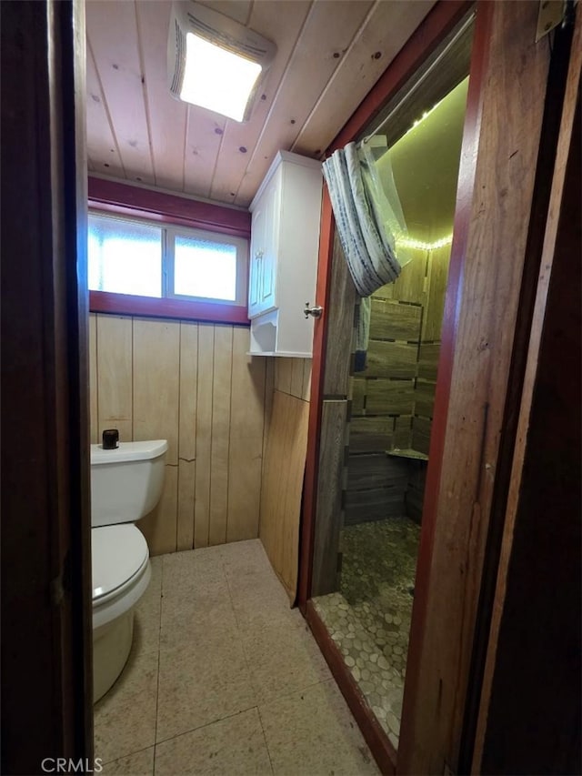 bathroom with wooden walls, wood ceiling, a tile shower, and toilet