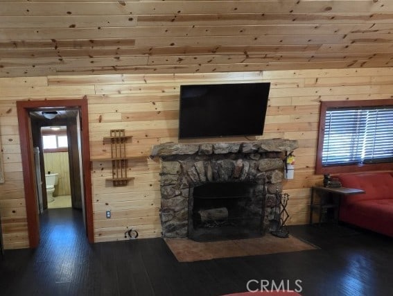 unfurnished living room with wood walls, a stone fireplace, and dark wood-style floors