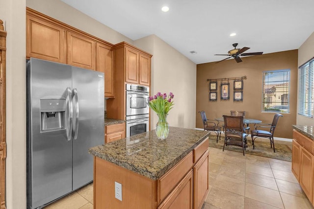 kitchen featuring light tile patterned flooring, dark stone counters, a center island, ceiling fan, and stainless steel appliances