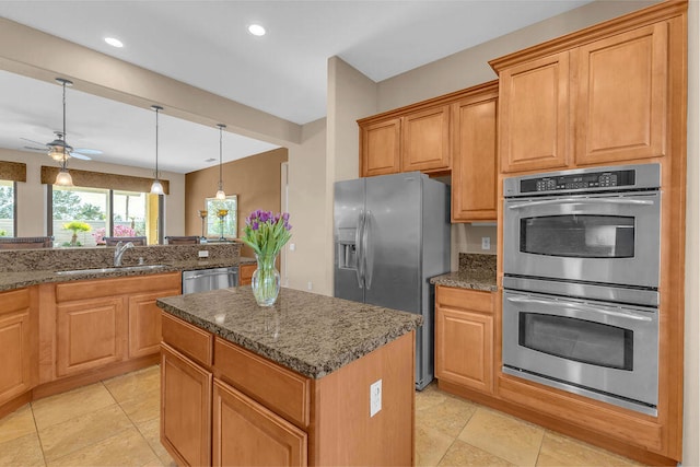 kitchen with sink, hanging light fixtures, appliances with stainless steel finishes, a kitchen island, and dark stone counters