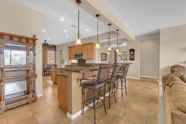 kitchen with light tile patterned flooring, dark stone countertops, a kitchen bar, hanging light fixtures, and beam ceiling