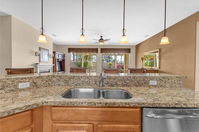 kitchen with sink, stainless steel dishwasher, pendant lighting, ceiling fan, and light stone countertops