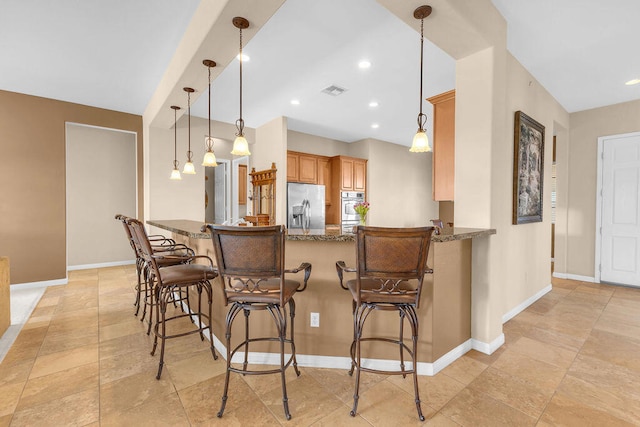 kitchen featuring stainless steel fridge, a breakfast bar area, dark stone countertops, hanging light fixtures, and kitchen peninsula