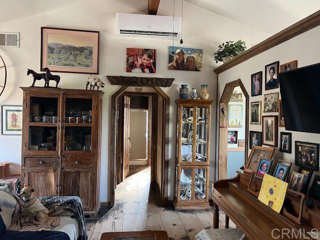 interior space featuring vaulted ceiling, a wall unit AC, and light hardwood / wood-style floors