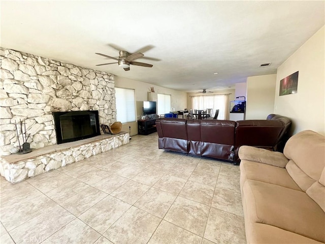 living area featuring ceiling fan, a stone fireplace, and light tile patterned flooring