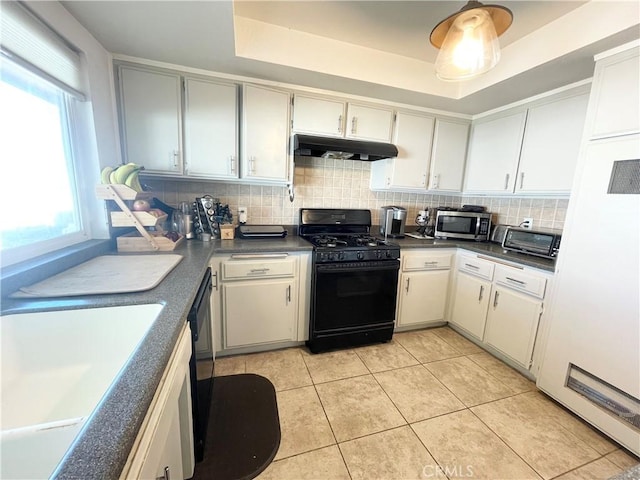 kitchen featuring black gas range oven, under cabinet range hood, stainless steel microwave, and a raised ceiling