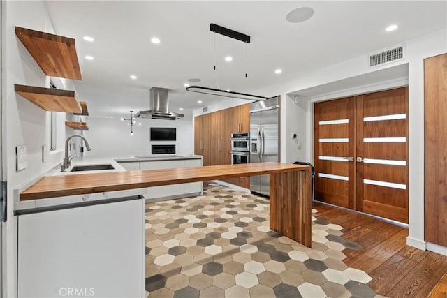 kitchen featuring sink, hanging light fixtures, stainless steel appliances, island range hood, and kitchen peninsula