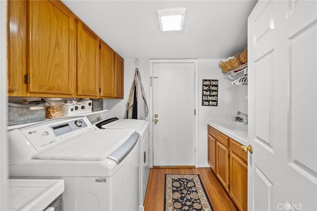 laundry area featuring cabinets, independent washer and dryer, sink, and light hardwood / wood-style flooring