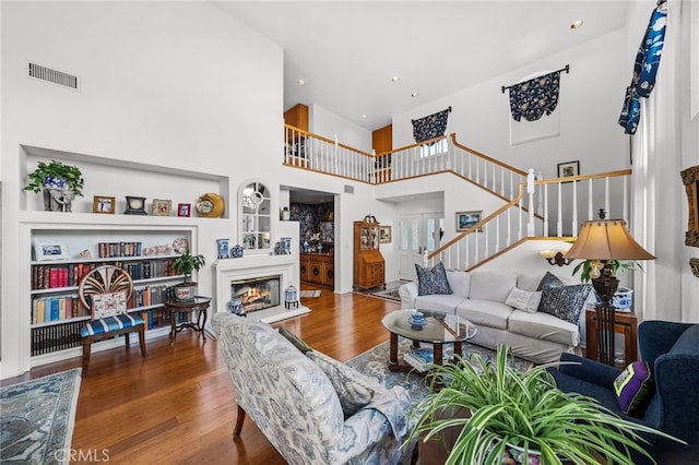 living room with hardwood / wood-style flooring, a towering ceiling, and built in shelves