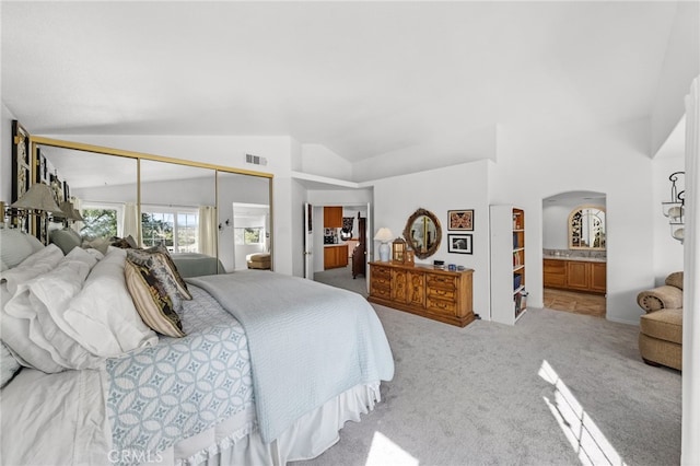 bedroom featuring a closet, ensuite bathroom, vaulted ceiling, and light carpet