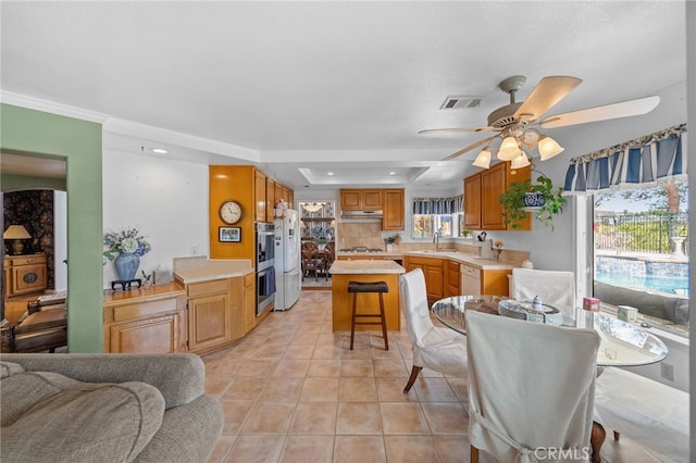 tiled dining area with a raised ceiling, sink, and ceiling fan