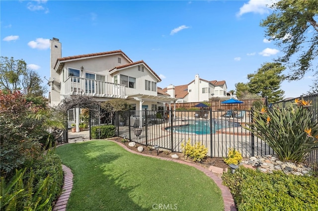 back of property featuring a balcony, a yard, a fenced in pool, and a patio