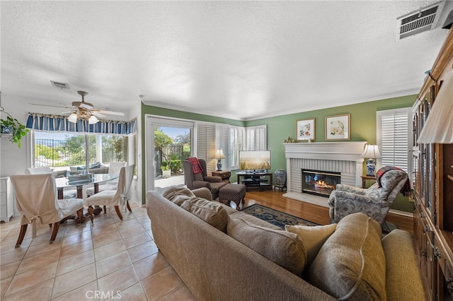 living room featuring light tile patterned flooring, a brick fireplace, ceiling fan, and a textured ceiling