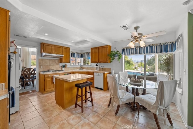 kitchen with a kitchen island, sink, white dishwasher, a raised ceiling, and a healthy amount of sunlight