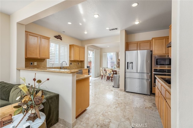 kitchen with sink, tasteful backsplash, light stone counters, appliances with stainless steel finishes, and kitchen peninsula