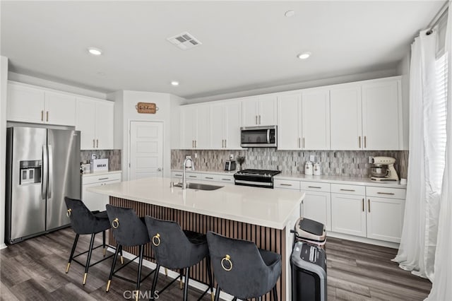 kitchen with appliances with stainless steel finishes, white cabinetry, sink, a kitchen bar, and a kitchen island with sink