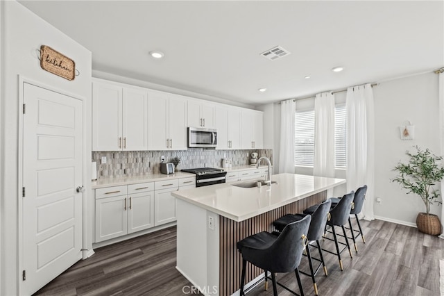 kitchen with sink, a breakfast bar area, white cabinetry, stainless steel appliances, and a kitchen island with sink