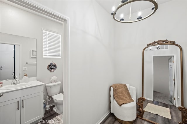 bathroom featuring vanity, wood-type flooring, toilet, and an inviting chandelier