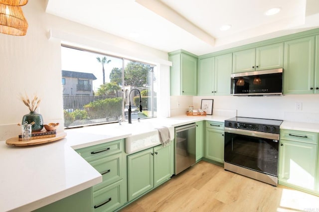 kitchen with appliances with stainless steel finishes, a tray ceiling, sink, and green cabinetry